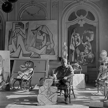 巴勃罗·毕加索（PABLO PICASSO）拿着一个农牧神的剪影，另一个农牧神坐在摇椅上。在巴勃罗·毕加索身后，有两幅画创作于1956年。加利福尼亚州洛杉矶，戛纳，1956年 – 爱德华·奎因–